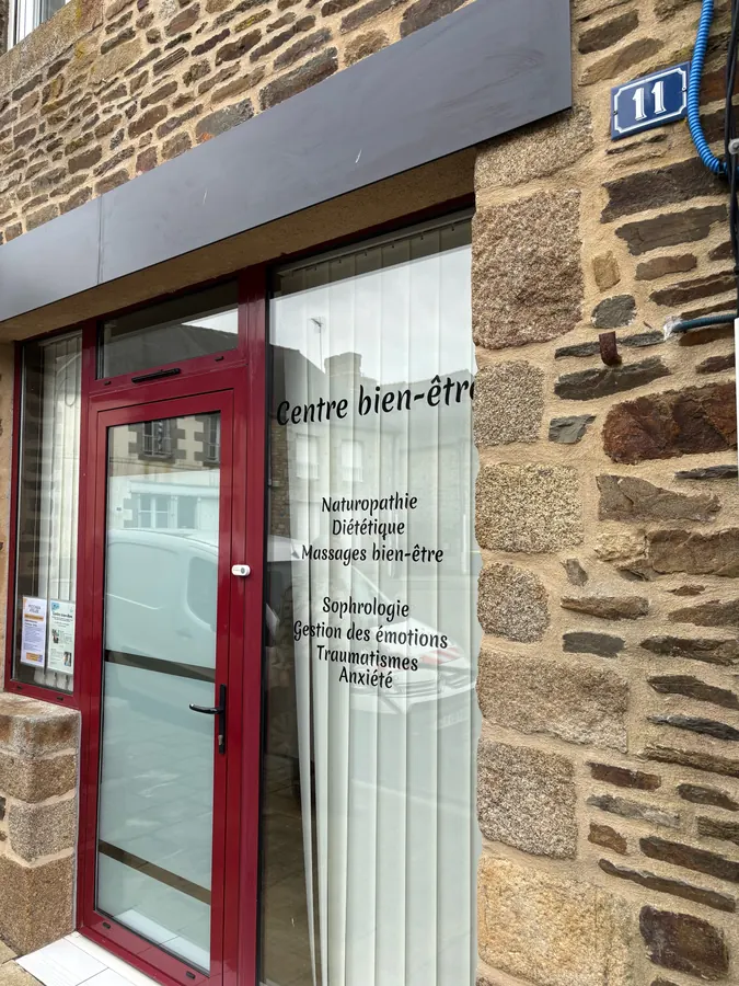 Façade en pierre du cabinet, porte rouge et vitrine « Centre bien-être »