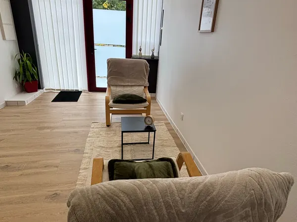 Pièce en longueur avec fauteuils à bascule et tapis, donnant sur une porte vitrée